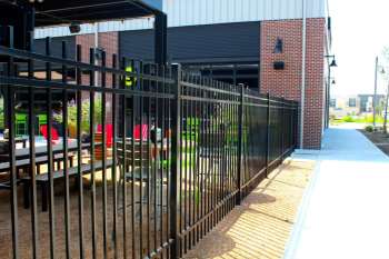 Black steel fencing enclosing shaded outdoor patio at Chicken N Pickle